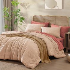 a bed with pink and brown comforters in a bedroom next to a plant on the wall