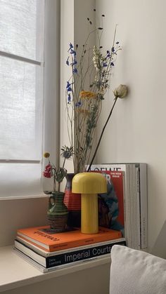 a stack of books sitting on top of a window sill next to a vase filled with flowers