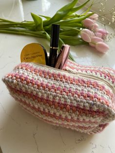 a crocheted purse sitting on top of a counter next to flowers and lipstick