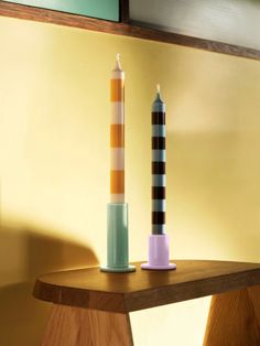 two different colored candles sitting on top of a wooden table in front of a yellow wall