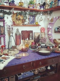 a purple table topped with lots of plates and bowls next to shelves filled with items