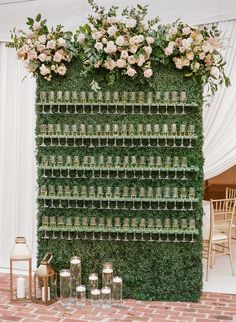 a green wall covered in lots of bottles filled with flowers and greenery next to candles