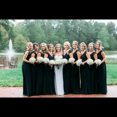 a group of women standing next to each other in front of a fountain holding bouquets