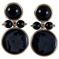 From Italy, a pair of 14-karat gold framed earrings with black onyx cabochons, beads, and carved armorial intaglios. Posted with backs. The upper bezels hold flat back cabochon cut, domed onyx stones, terminating with two pinned and capped onyx beads. The pins hold a swinging, bezeled carved onyx stone, each showing a different Roman helmeted warrior head. Measures: 1 inch Long (25.4 mm) x .75 inch Wide (19.05 mm) .50 inches from front to end of post. Intaglios: .50 inches diameter (12.7 mm) Top Regulus Black, Jeweled Earrings, Onyx Bead, Onyx Stone, Gold Frame, Black Onyx, Onyx, Cufflinks, Jewelry Collection