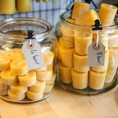 two glass jars filled with yellow candles on top of a wooden table next to each other