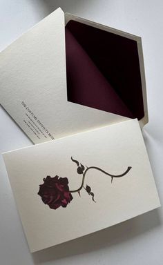 an open box with a rose on it sitting next to a white envelope and card