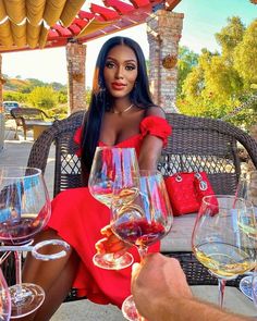 a woman in a red dress sitting at a table with wine glasses