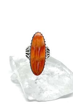 This sterling silver Orange Spiny Shell Ring by Navajo artist, Delbert Vandever, showcases the perfect color of orange to add to your wardrobe. A long oval shape makes fingers appear longer and slimmer. The handmade smooth bezel surrounding the stone and the sturdy split shank band add to the contemporary style. This is a stunning example of modern Navajo jewelry. Orange Spiny Shell is found deep in the Sea of Cortez in the Baja region of the Gulf of California. Handmade in New Mexico. Hallmarke Orange Oval Ring With Polished Finish, Oval Orange Ring With Polished Finish, Southwestern Oval Jewelry With Polished Finish, Southwestern Style Oval Jewelry With Polished Finish, Orange Oval Jewelry With Polished Finish, Oval Orange Polished Jewelry, Orange Oval Sterling Silver Jewelry, Unique Oval Orange Jewelry, Orange Oval Sterling Silver Ring