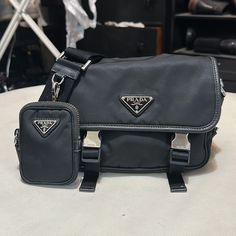 Prada Re-Nylon And Saffiano Leather Shoulder Bag Unisex Also Posted Hat Separately M Nice Conversation/ Status Piece Great Bag, Preserved Very Well Reduced Price Due To Minor Flaws Comes With Box Taking Offers - Small Pouch Zipper Fading( No One Pays It Any Attention)As Shown In Pic. I Had Small Pouch Hook Strap Reinforced To Keep From Tearing Away From The Leather( Also Unnoticed)As Shown In Pic Waiting For A New Home Classic Black Shoulder Bag With Silver-tone Logo, Designer Black Shoulder Bag With Silver-tone Logo, Designer Black Bag With Silver-tone Logo Plaque, Designer Black Bag With Silver-tone Logo, Luxury Black Shoulder Bag With Silver-tone Logo, Small Pouch, Small Pouches, Zipper Pouch, Leather Shoulder Bag