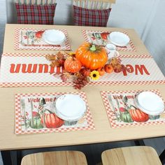 a wooden table topped with white plates and orange pumpkins on top of checkered napkins