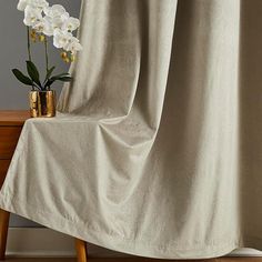 a vase with flowers sitting on top of a wooden table next to a drapes