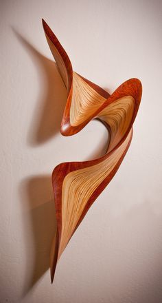 a wooden sculpture is hanging on the wall in front of a white wall and it looks like an abstract piece of art