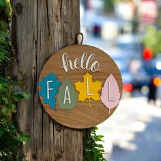 a wooden sign that says hello fall hanging on a tree in front of a city street