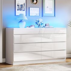 a white dresser with blue lights and pictures on the wall