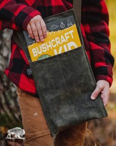 a person holding a bag in their left hand and wearing a red plaid shirt with the word bushcraft on it