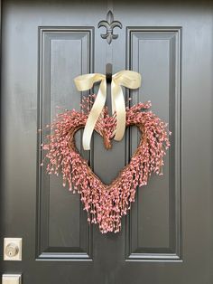 a heart shaped wreath is hanging on the front door with pink flowers and white ribbon