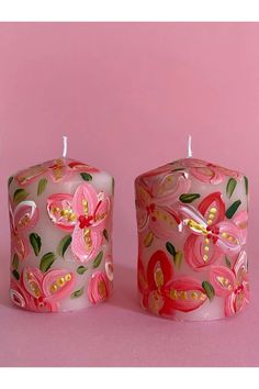 two pink candles sitting next to each other on top of a pink surface with flowers painted on them