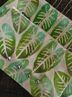 a green and white leaf print fabric with metal beads on a wooden table next to a chain