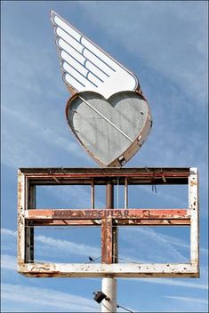 a heart shaped sign on top of an old metal pole with a sky in the background