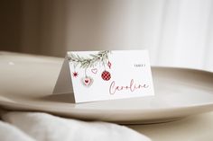 a place card is placed on a plate with white linens and christmas decorations around it