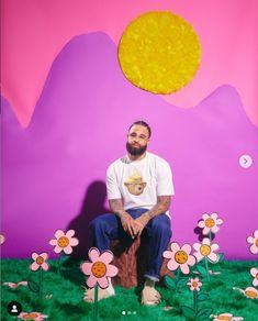 a man sitting on top of a tree stump in front of a field of flowers