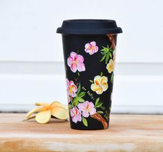 a black coffee cup sitting on top of a wooden table next to a yellow flower