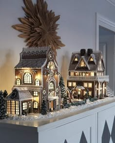 a christmas display with lit up houses and trees on top of the mantle in front of a window