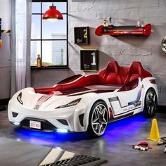 a white sports car bed with red seats and blue lights on the floor in a room