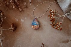 "This piece of nature inspired jewelry is designed to look like it encases tiny mountains set in front of a colorful iridescent galaxy. The pendant is shaped and polished by hand from natural wood, resin and lab-made opal. The high quality finish makes the wood silky smooth and the resin glass like. The piece shown in the picture is to show the shape, color and style of the pendant you are buying. There may be slight variation in the color and appearance of the pendant you receive as each piece Wood Resin Necklace, Unique Opal, Blue Opal Necklace, Mountain Necklace, Rainbow Opal, Resin Ideas, Necklace For Her, Nature Inspired Jewelry, Resin Necklace