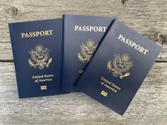 three us passports sitting on top of a wooden table with the word passport written in gold