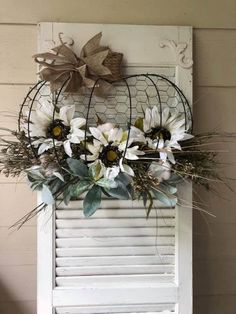 an old shutter is decorated with white flowers and greenery in front of a window