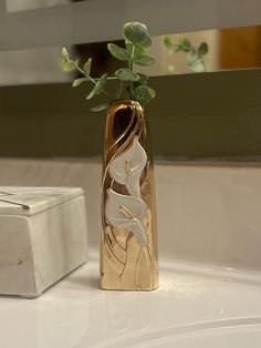 a gold vase with a flower in it sitting on a white counter next to a mirror