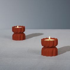 two red candles sitting on top of a white table next to each other in front of a gray background