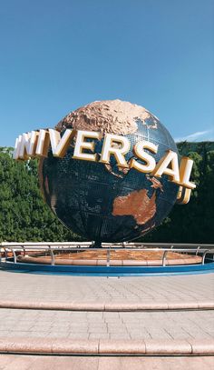 a large metal sign that says universal on top of a giant globe with trees in the background