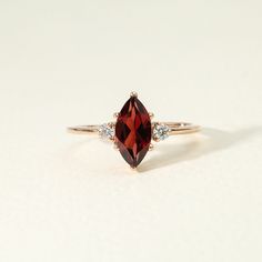 a close up of a ring with a red stone and two white diamonds on it