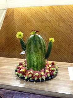 a green cactus sitting on top of a wooden table next to a pile of fruit