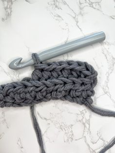 a crochet hook is laying on top of a white marble counter with gray yarn