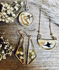 three necklaces with flowers and birds on them sitting on a table next to dried flowers