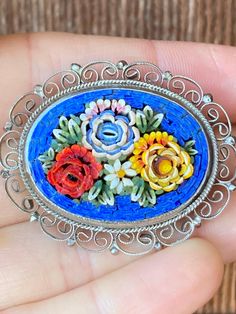 This is one of the prettiest micro mosaics I have come across with its bright colors and raised petal design. The flowers are two toned with golden orange, blue and red as the predominant colors and a little white daisy in the pattern. The blue border is bright and deep and the raised pieces really add depth and unique dimension to the brooch.  The setting is silver toned and the border has pretty see through filigree. The back is unmarked and the brooch measures 1 1/2 inches long. Antique Multicolor Brooch For Gifts, Antique Multicolor Brooches As Gifts, Multicolor Cabochon Brooch As Gift, Multicolor Cabochon Brooch For Gift, Multicolor Cabochon Brooches As Gift, Multicolor Cabochon Brooches For Gifts, Multicolor Cabochon Brooches For Collectors, Unique Multicolor Cabochon Brooches, Handmade Multicolor Flower Brooch