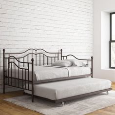 a day bed sitting on top of a wooden floor next to a white brick wall