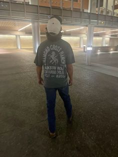 a man walking in an empty parking garage with his back to the camera and wearing a baseball cap