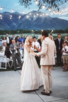 a bride and groom holding hands during their wedding ceremony in front of an outdoor crowd