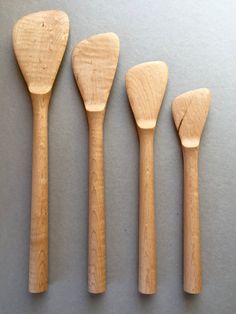 four wooden spoons lined up next to each other on a gray surface with white background