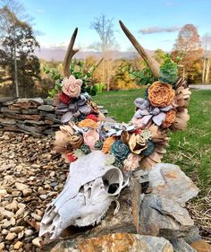 an animal skull with flowers on it is sitting on some rocks in the grass next to a rock wall