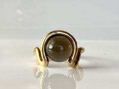 Bold, modern and striking in its distinctive design and craftsmanship, this earthy grey moonstone round cabochon ring is a contemporary alternative to the traditional cocktail ring. Slip this ring on your finger when you need a bold, statement-making piece of jewelry. 9K solid yellow gold  Grey moonstone 11mm Available size 18.4 Follow us on Instagram: https://www.instagram.com/missionewyork/ Modern Yellow Gold Round Moonstone Ring, Modern Cabochon Moonstone Ring For Formal Occasions, Modern Round Cabochon Moonstone Ring, Modern Cabochon Moonstone Ring, Modern Moonstone Ring With Oval Cabochon, Modern Yellow Gold Moonstone Ring, Grey Moonstone, Gold Statement Ring, Wave Ring