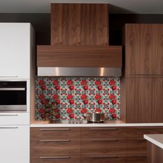 a kitchen with wooden cabinets and white countertops has red flowers on the backsplash