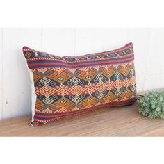 an orange and blue pillow sitting on top of a wooden table next to a potted plant