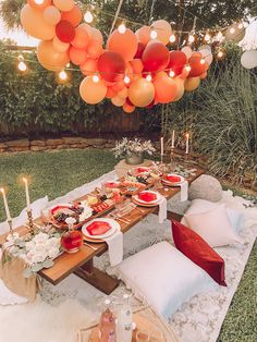 an outdoor table set up for a party with orange and white balloons hanging from the ceiling