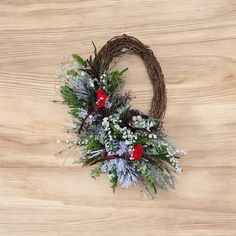 a wreath with red flowers and greenery on a wooden surface, ready to be used as an ornament