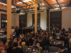 a large group of people sitting at tables in a room with chandeliers on the ceiling